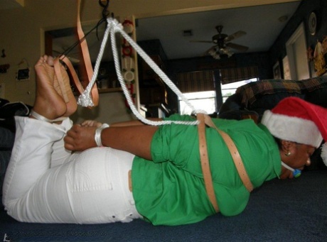 A weighty black woman is ball gagged while being tied up in a Santa costume.
