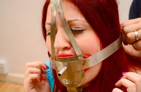 Wearing a medieval-looking gag, the pale redhead is tucked in place with a chain.