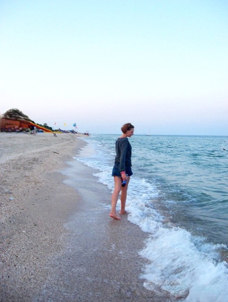 Red haired amateur girl steps into the ocean and swims in a bikini before going swimming.