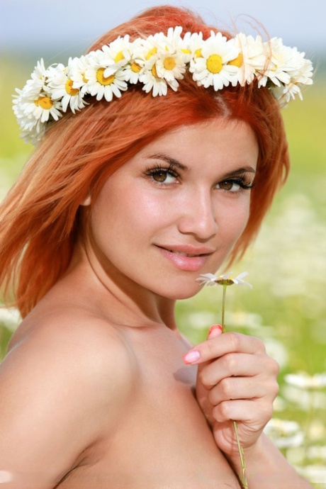 Dina P, a stunning redhead, is seen wearing a crown of daisies and naked in a field.