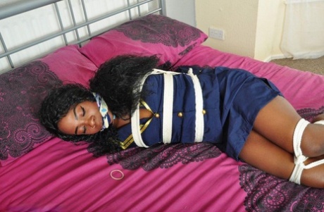 In her uniform, the Ebony stewardess is left tied up and gagged on a bed.