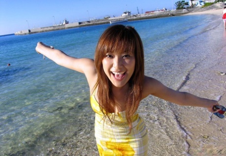 A delightfully cute Asian model happily poses on the beach while flaunting her tight tits.