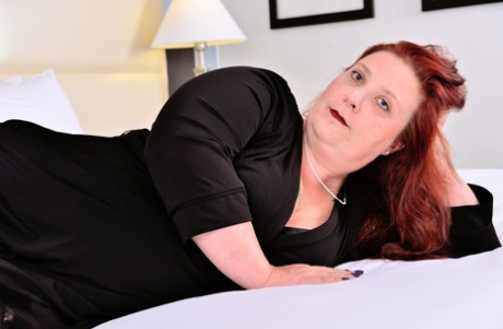 The overweight body of Nikki Hayze, an elderly Canadian redhead, is exposed on a bed.