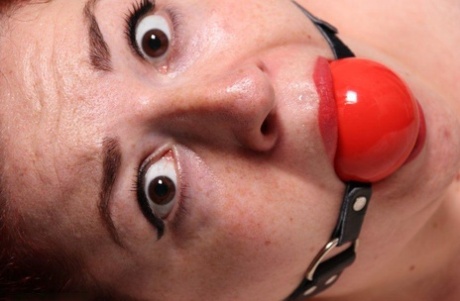 Thin reds are tied loose in her panties while sporting a big ball gag.