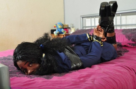 A bed is where a black female stewardess is found crawling and bound in a hogtied position.