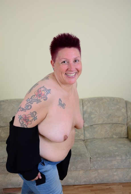 The overweight tattoo girl flaunts her chest and abs while wearing blue jeans.