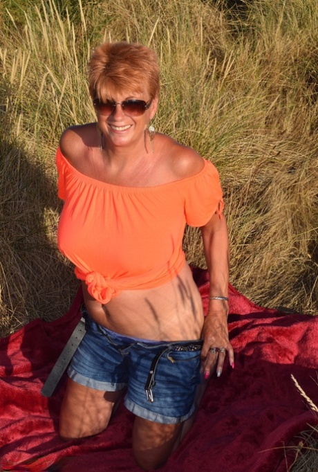 A fit and elderly woman named Dimonty exposes large natural phenomena on a blanket that overlooks the ocean.