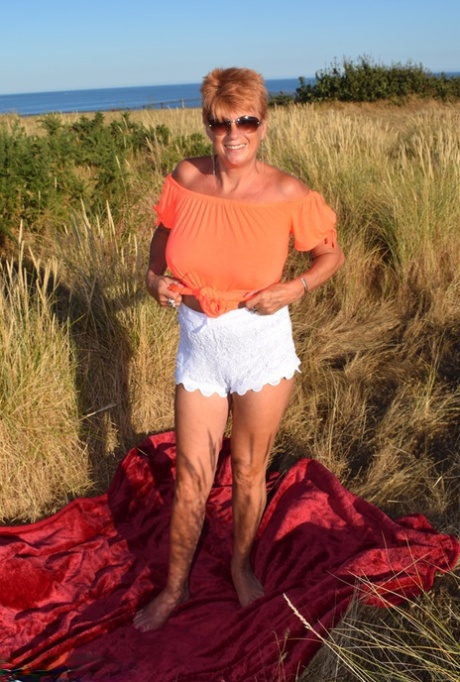 Dimonty, a fit elderly woman who is also tall, exposes large natural wonders on a blanket that overlooks the ocean.