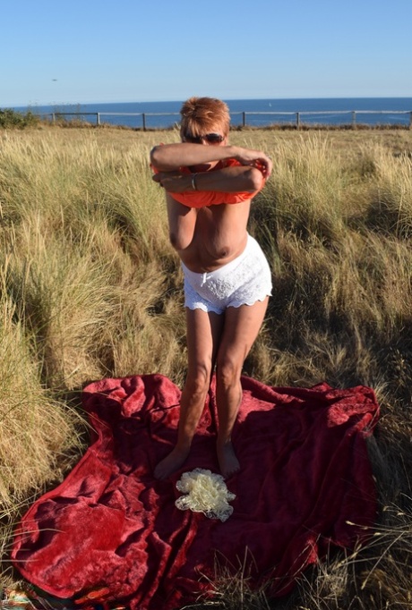 Dimonty, an aged and healthy woman, exposes large natural wonders on a blanket that overlooks the ocean.