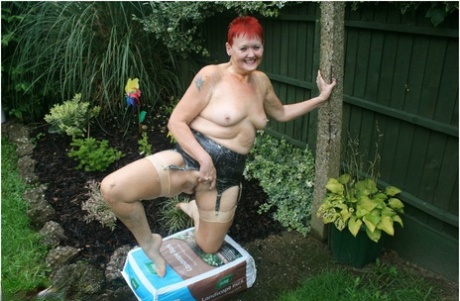 Dressed as a redhead granny, Valgasmic Exposed poses naked in a yard with nylons on her back.