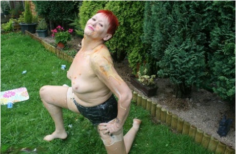 Valgasmic Exposed, the redhead granny, is seen in a yard with nylons on her body while being nude.