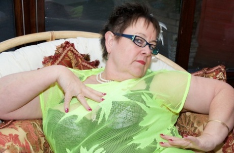 A fat, slick-haired older woman with short spiky hair playsfully grabs her glasses while playing.