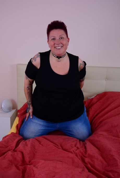 The overweight tattoo girl lets her breast escape from her bra while lying on a bed.