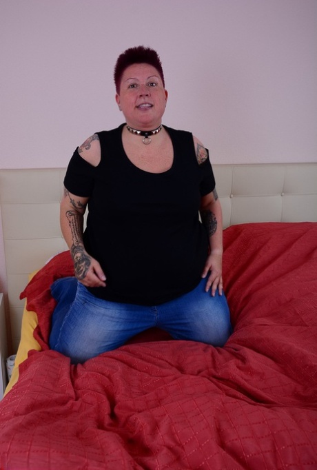 A tattoo girl who is overweight lets a breast escape from her bra while lying on a bed.