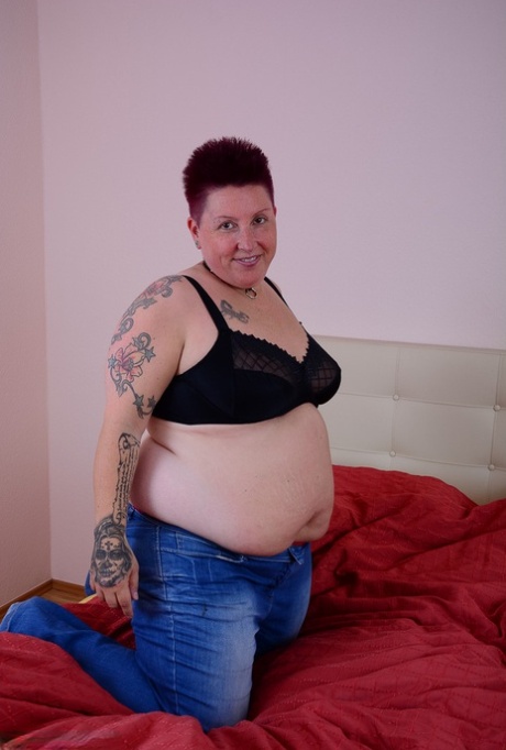 This overweight Tattoo Girl lets a breast drain out of her bra while lying on the bed.