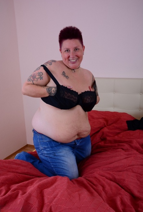 An obese tattoo girl who is an amateur lets a breast slip out of her bra while resting on a bed.