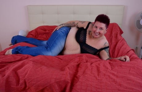 A tattoo girl who is overweight allows her breast to spill out of the bra while sitting on a bed.