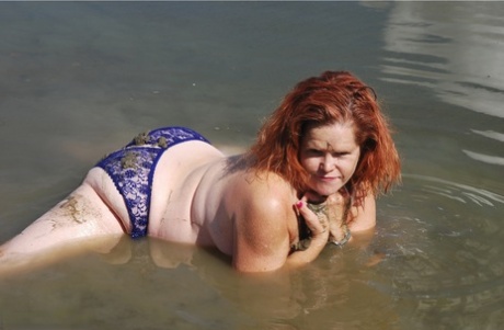 In shallow water, Misha with red hair covers her big tits with mud.