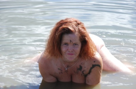 Redheaded amateur Misha dips into mud while swimming in shallow water on her big tits.