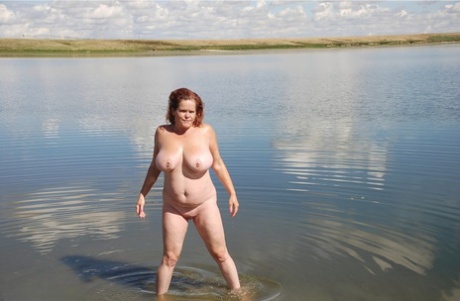 Redheaded amateur Misha dips into mud while swimming in shallow water on her big tits.