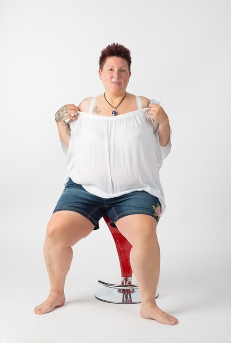 Толстая татуированная девушка сидит на табуретке после того, как полностью обнажилась