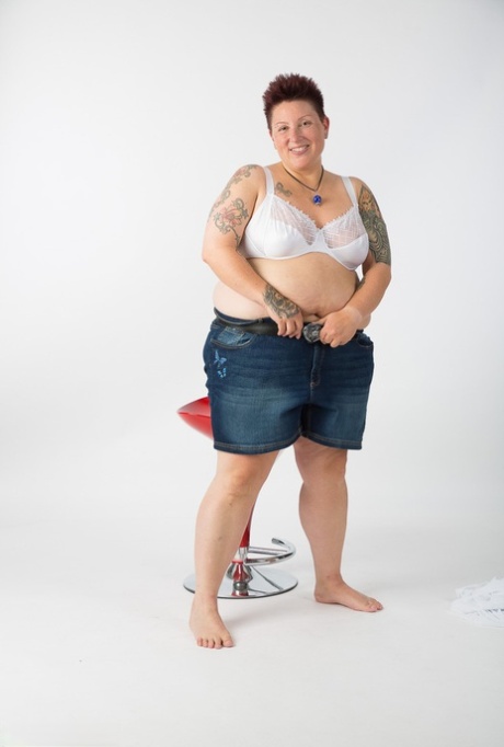 Completely unclothed, the elderly Tattoo Girl takes a seat on a stool after getting naked.