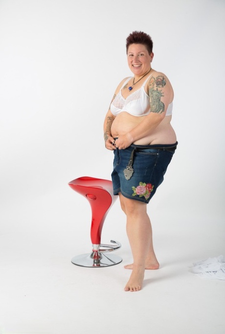 An unclothed Tattoo Girl who is an obsessive tattoo artist takes a seat on a stool after getting completely nude.