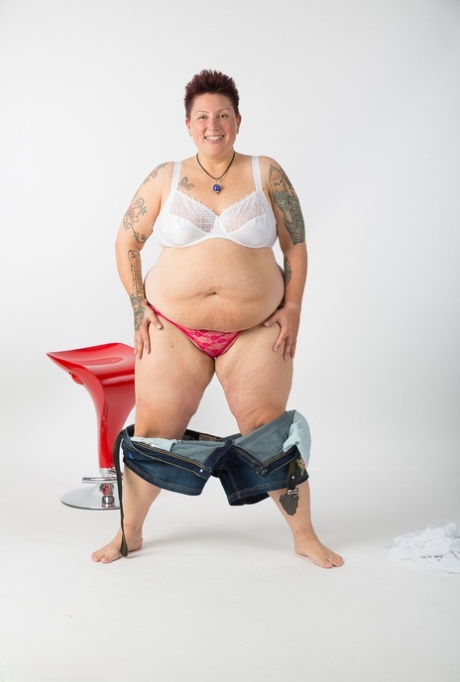 Unclothed and unmarried Tattoo Girl, who is an elderly woman, sits on a stool after getting completely naked.