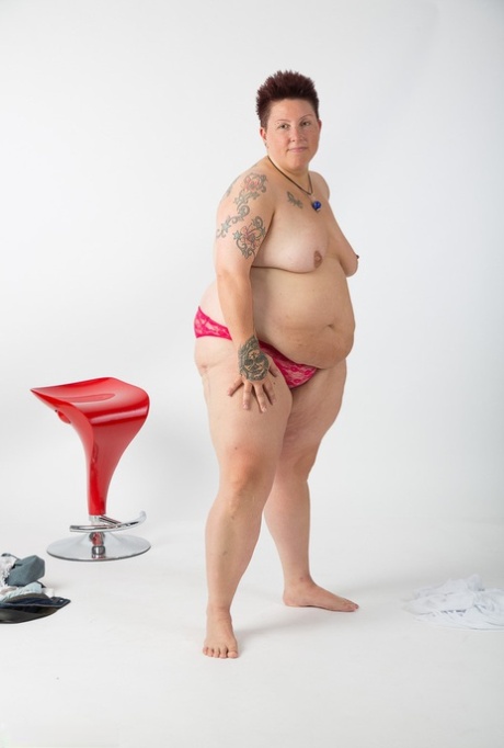 Following her complete nudity as an amateur tattoo artist, the elderly woman sits on a stool.