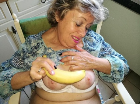 In her natural pussy state, Horny granny Caro clings to a banana while sitting on the kitchen chair.