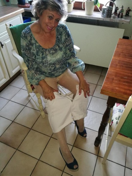 Horny granny Caro, who is tall, inserts a banana into her natural pussy on the kitchen chair.