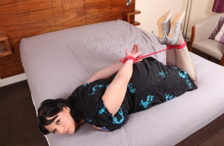 A fully clothed brunette is left tied up and gagged on a bed.