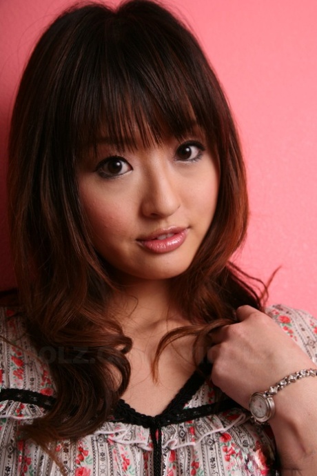 Against a pink wall, an attractive Japanese model is seen with her clothes on.