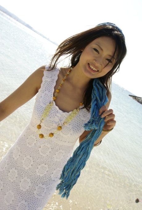 In the middle of the ocean, an Asian girl dresses in a white dress and walks to her knees.