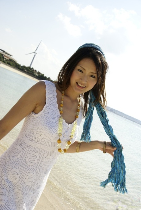 Wearing a white dress and dancing in the water, an Asian girl ventures into the ocean to her knees.