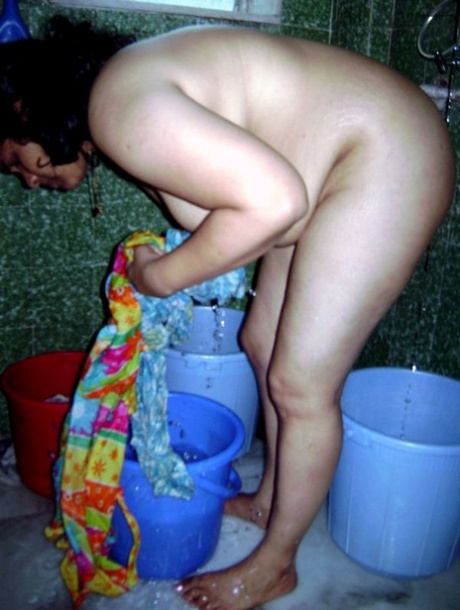 A fatty woman from India is washing her clothes and taking out a shower at the same time.