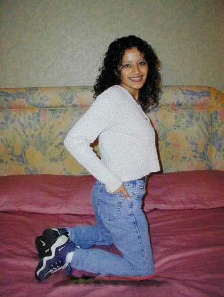 The Latina woman with curly hair reveals her exposed rear end on a bed.