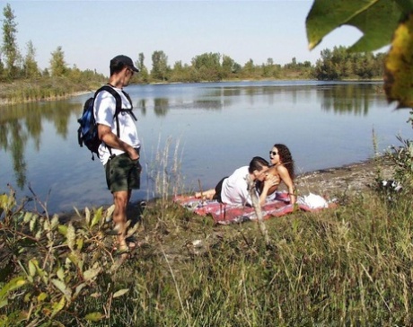 A horny pair engages in sexual activity near the water with a hiker, enjoying the sex.