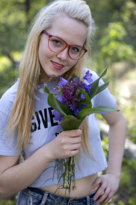 Nika the blonde with nerdy hair, is naked and holding a bunch of wildflowers on top of a log.