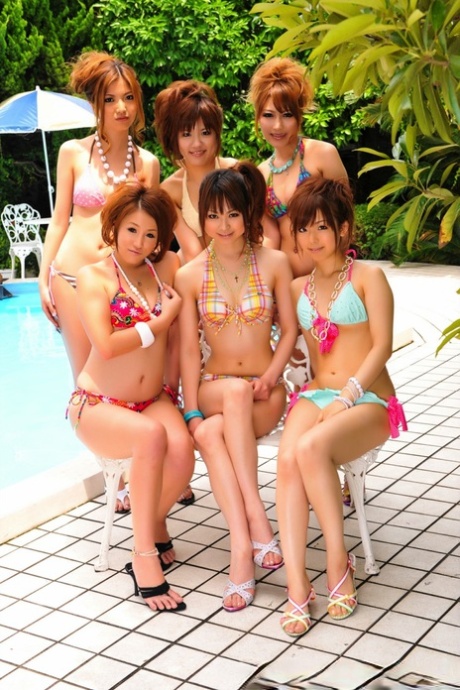 A group of Japanese bikini models gather on a poolside patio for a group photo shoot.