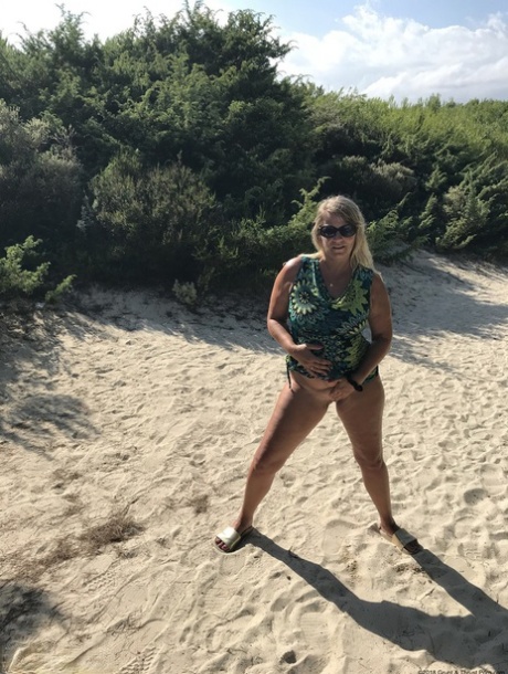 Sweet Susi, a fat midget, taps her buttocks on a sandy dune and then cups them in the air.