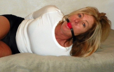 In a bed in black miniskirts, a little-known blonde MILF is held tightly and ball gagged.