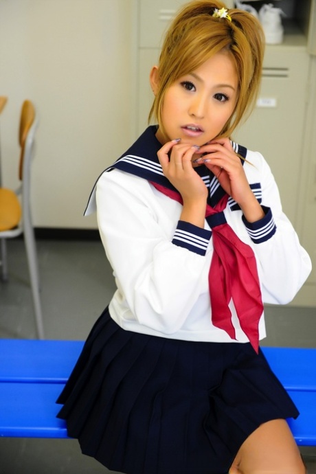 Adorable Japanese student, with a charming face, sits on top of the bench in her uniform.