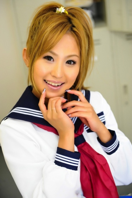 An adorable young woman from Japan poses for a photo on the bench in her uniform, complete with a cute face.