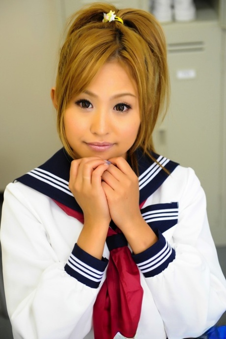 An attractive Japanese girl with a lovely face sits on a bench in her uniform.