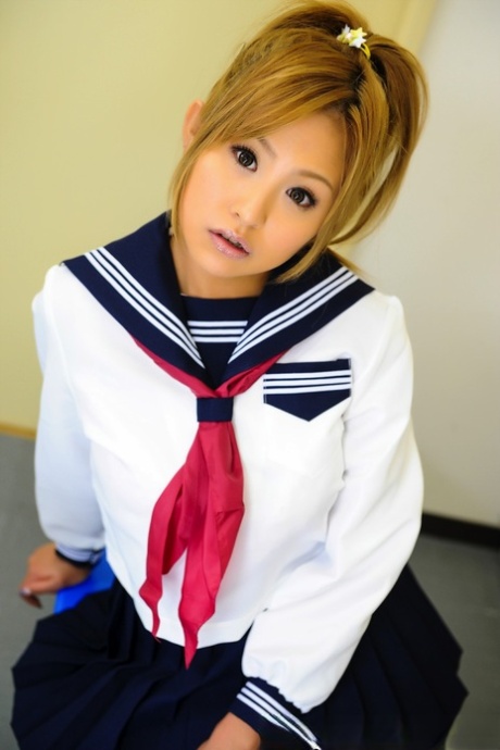 Adorable Japanese student with a charming face sits on a bench in her uniform.