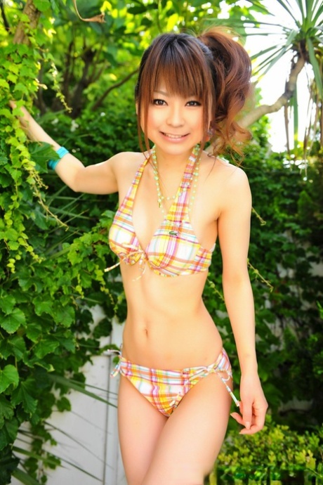 A bikini is being modeled by an Asian girl who wears her hair in a ponytail near a pool.