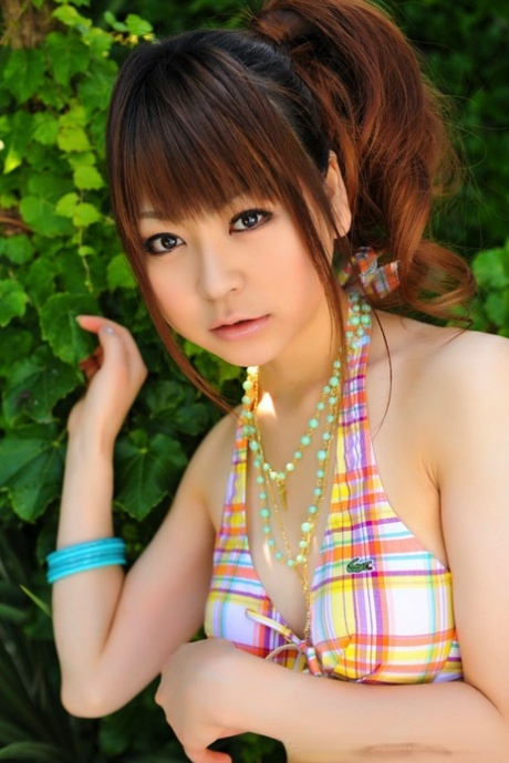 At the pool, a small Asian lady models her hair in ponytails while wearing a bikini.