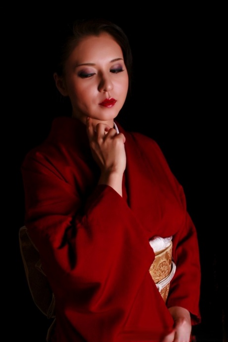 While wearing traditional clothing, the Japanese woman displays red lips while holding a knife.