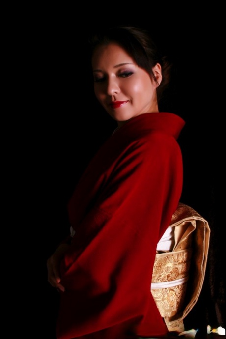 During her traditional attire, the Japanese woman wears red lips while holding up a knife.